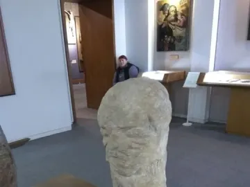 Škloŭ Idol stone sculpture displayed on a wooden stand in a museum gallery.