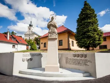Stone statue of St. John of Nepomuk holding a crucifix, standing on a pedestal with a halo of stars around his head.