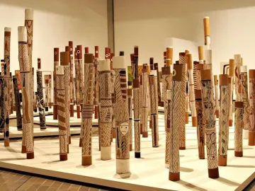 Aboriginal Memorial sculpture made up of numerous decorated wooden poles standing upright on a light-colored platform.