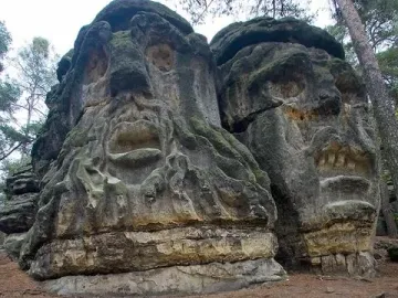Devil\'s Heads sandstone carvings in a forest, showing two large stone faces on the outcrop.