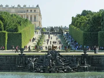 Neptune Fountain in Versailles with mythological sculptures and cascading water, set before a formal garden path leading toward the palace.