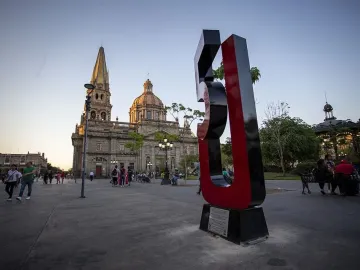 Antimonumento 5J standing on a paved plaza with a historic church and spires in the background.