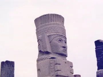 Tall stone Atlantean figure at Tula with an elaborate headdress and stylized face, seen against a bright sky.