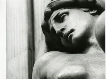 Reclining marble figure of Dawn with a downcast expression and bare shoulder and breast.