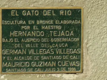 Green commemorative plaque with raised metal lettering mounted on a textured wall.