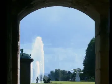The Emperor Fountain seen through a stone archway, with a tall water jet rising above a green lawn.