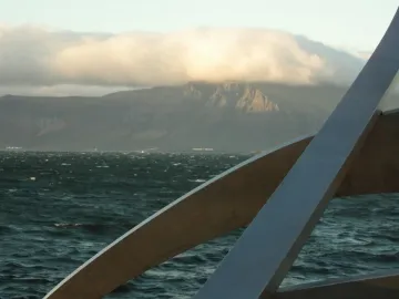 The Sun Voyager sculpture in the foreground with dark water and distant mountains under cloudy skies.