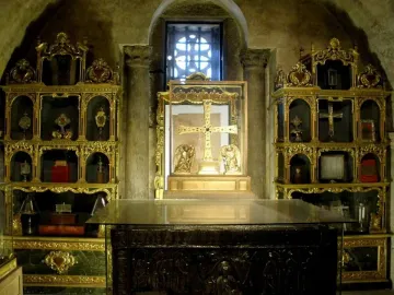 The Cross of the Angels displayed upright in a glass case with two golden figures at its base.