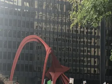 Flamingo sculpture in red steel rising above a crowd in front of a dark building with reflective windows.