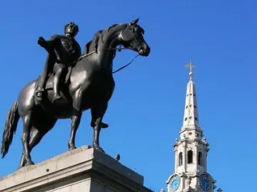 The Equestrian Statue of George IV silhouetted on its pedestal against a blue sky, with a church steeple nearby.