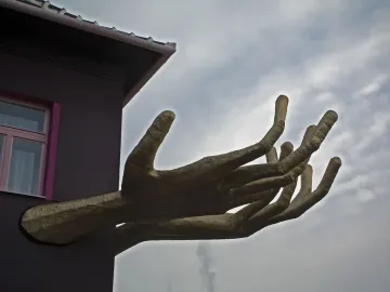 Golden sculptural hands extend from the corner of Kristek House beside a pink-framed window.