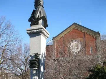 La mort de Dante monument with a dark statue on a tall stone pillar in a snowy park.