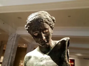 The Cleveland Apollo bronze statue bust with green patina and pale inlaid eyes inside a museum hall.