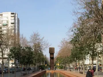 El Llarg Viatge at the end of a long reflecting pool, with trees, buildings, and people mirrored in the water.