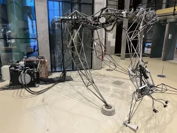 The Senster robotic sculpture with a skeletal metal framework, cables, and jointed limbs beside a separate machinery unit.