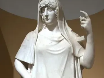 Giustiniani Hestia, a white marble female statue in draped garments with one hand on her hip and the other raised.