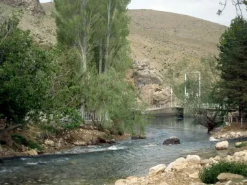 The Ivriz relief carved into a rock face beside the river, with a white railing along the base.