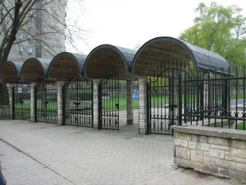Monument of Common Martyrdom with four arched structures, stone pillars, and wrought-iron gates beside a walkway.