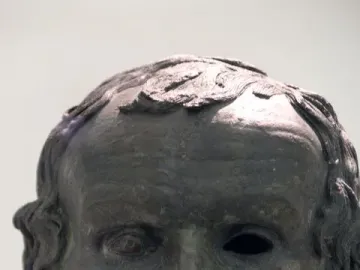 The Porticello Head bronze sculpture of an older man with a wavy beard and hollow eyes on a pedestal.