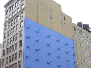 The Wall sculpture on a bright blue building facade with rows of teal projections above a beige lower section.