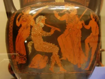 Red-figure ceramic vase showing a seated satyr playing a double flute, with other figures around him.