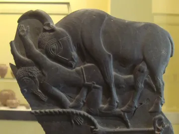 Bull Palette carved relief showing a large bull over human figures with a woven border at the bottom.