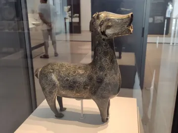 Ciervo de Madinat al Zahra, a bronze-colored deer sculpture with circular patterns, displayed in a museum case.