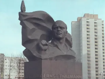 Ernst Thälmann Memorial bronze bust with a clenched fist and banner-like sculpture on a pedestal in a snowy urban setting.