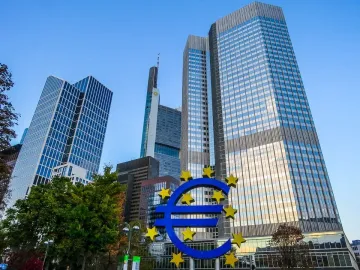 Blue Euro sculpture with yellow stars in front of modern glass skyscrapers.