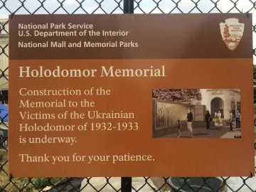 National Park Service sign about Holodomor Memorial construction on a chain-link fence