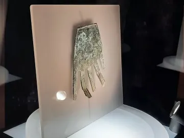 The Hand of Irulegi metal artifact displayed behind glass on a light panel.