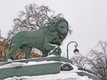 Lions at the Dvortsovaya Pier lion statue with a paw on a sphere, standing on a snow-covered pedestal.