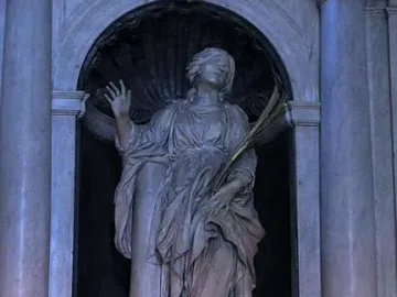 St. Bibiana marble statue in an arched niche, holding a leafy frond and raising one hand.