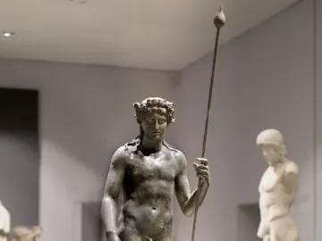 Tiber Dionysus bronze statue of a standing nude male figure with a wreath and staff in a museum.