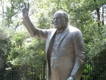 Winston Churchill statue making a V-for-Victory sign with one hand and holding a cane.