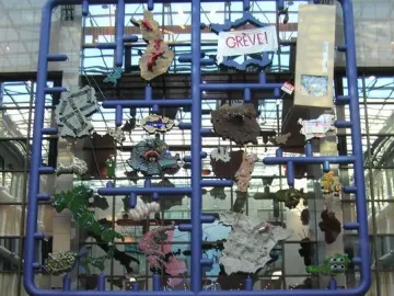 Entropa installation with a large blue grid frame and colorful attached shapes in a modern interior, with people gathered below.