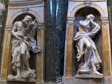 Saints Jerome and Mary Magdalen marble statues in arched niches with dark columns, showing Jerome holding a cross and Magdalen gazing upward.