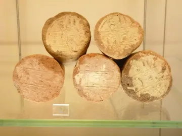 Five terracotta funerary cones with worn impressed inscriptions, displayed on a glass surface.
