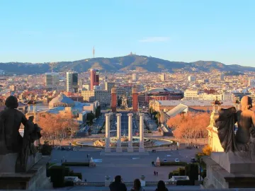 The Four Columns standing in a plaza with a circular fountain in front and a city and mountains in the distance.