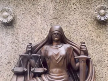 Bronze relief sculpture of Lady Justice seated with scales and a sword on a stone wall.