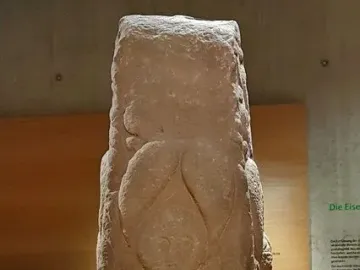 Pfalzfeld Obelisk, a weathered carved stone column displayed on an orange platform in a museum.