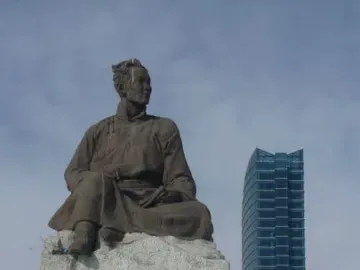 Natsagdorj Monument, a bronze statue of a seated man in traditional attire on a stone base, with a modern glass building behind it.