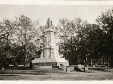 Peace Monument with sculpted figures and a statue at the top, standing among trees in a park-like setting.