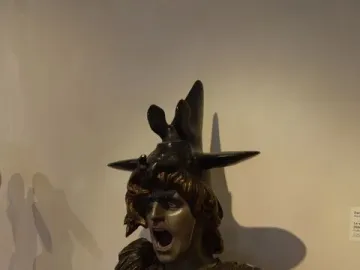 Bronze bust of Bellona with an anguished expression, wearing a helmet and ornate armor with a blue jewel.