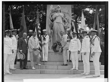 Commodore John Barry statue monument with men gathered on the steps and flags around it.