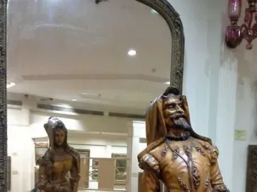 Mephistopheles and Margaretta wooden sculpture showing a bearded male figure, with the female side visible in the mirror behind it.