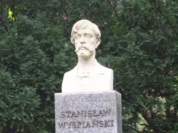 Stanisław Wyspiański bust on a tall granite pedestal surrounded by green foliage.
