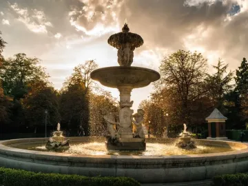 Fountain of the Artichoke in a park, with water cascading from the stone tiers into a circular pool at sunset.