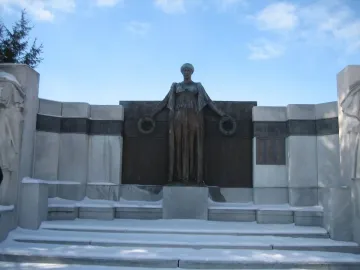 Soldiers\' Monument bronze figure holding wreaths in front of a curved stone structure with snowy steps.