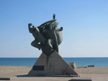Monument of Eupatoria Assault bronze sculpture with three figures on a stone base by the sea.